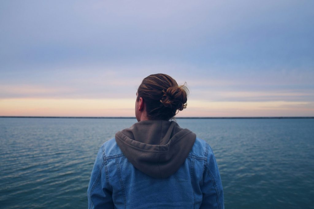 Frau in blauer Jeansjacke steht tagsüber in der Nähe eines Gewässers